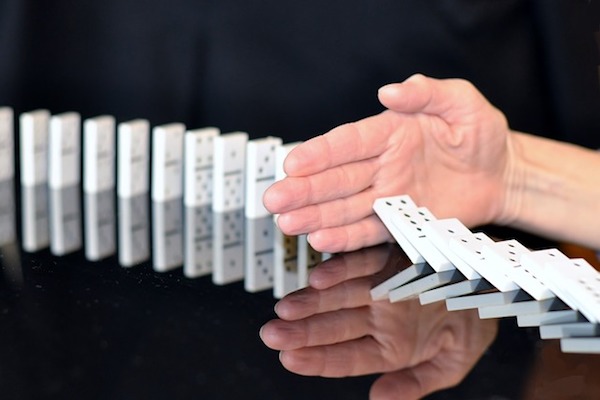 Externalidades simbolizadas pela queda dos dominós interrompida por uma mão